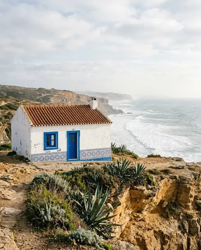 Casa branca com barras azuis sobre as arribas da Ericeira, oceano ao fundo